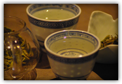 the liquor in two little ceramic cups flanked by the infusion in the glass pot and dry leaf in the ginkgo dish